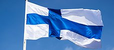 En finsk flagga som vajar i vinden mot blå himmel